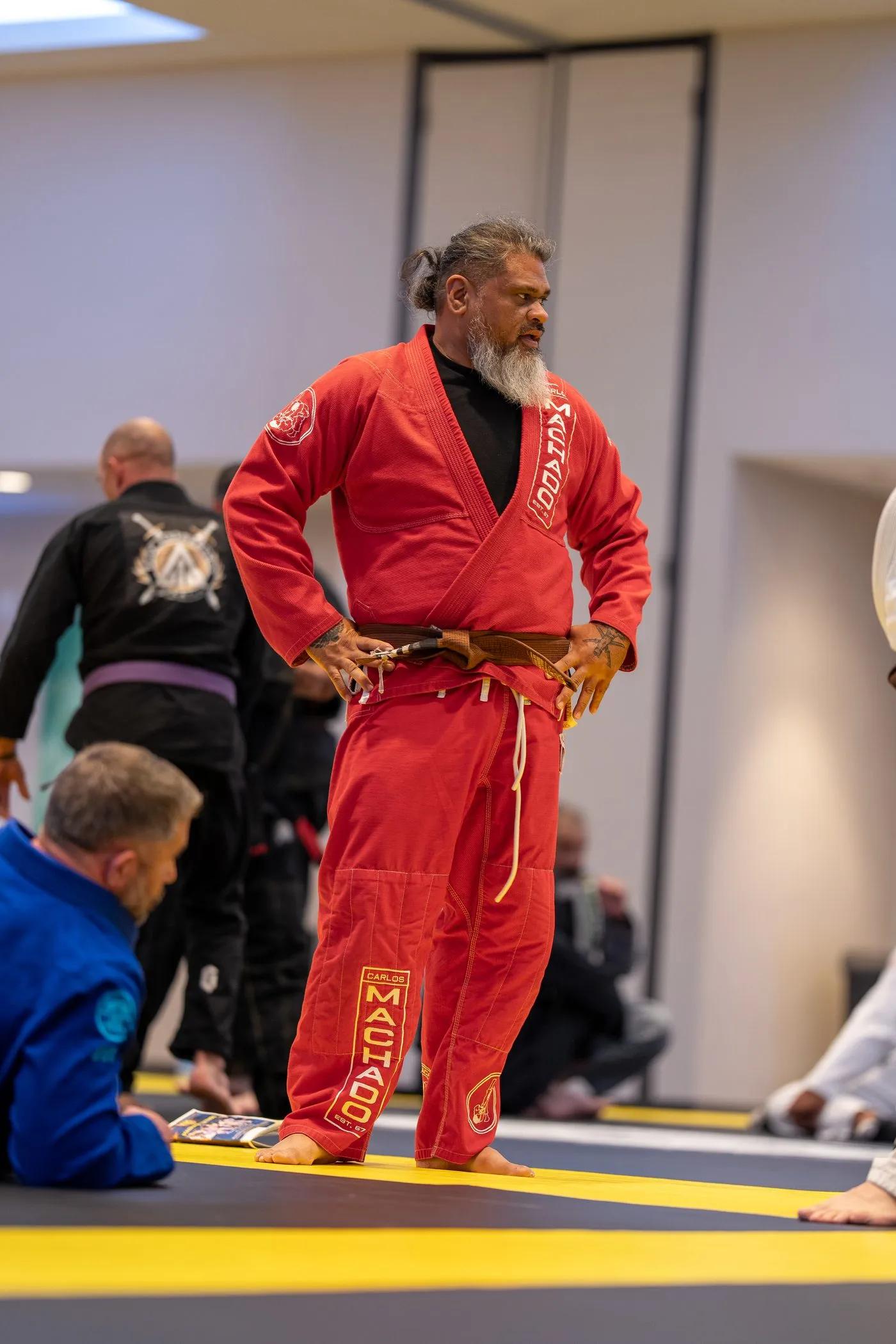 A senior instructor in a red Machado gi standing at the edge of the mat