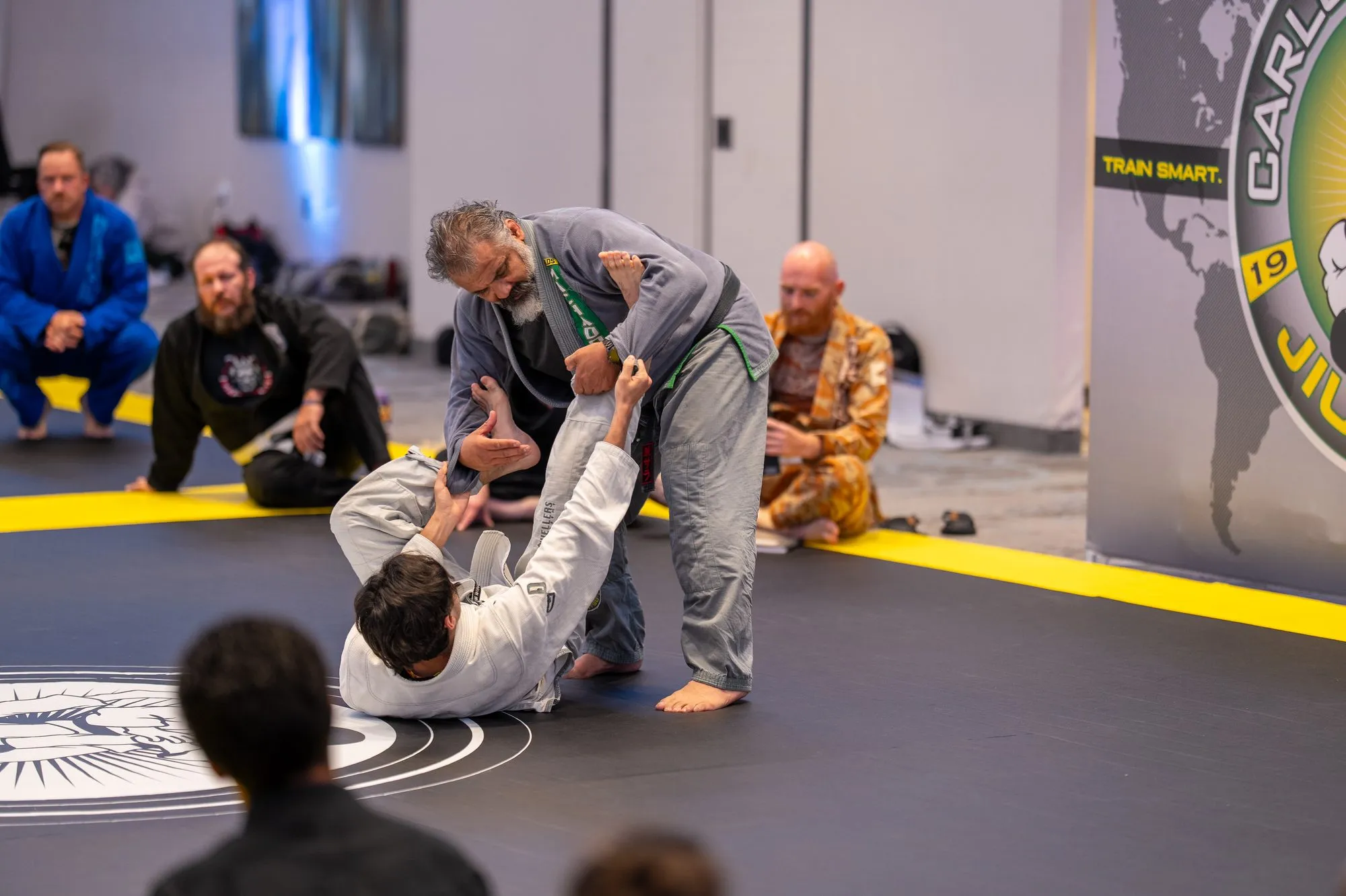 Two practitioners in gis drilling beside the Carlos Machado Jiu-Jitsu world-map banner