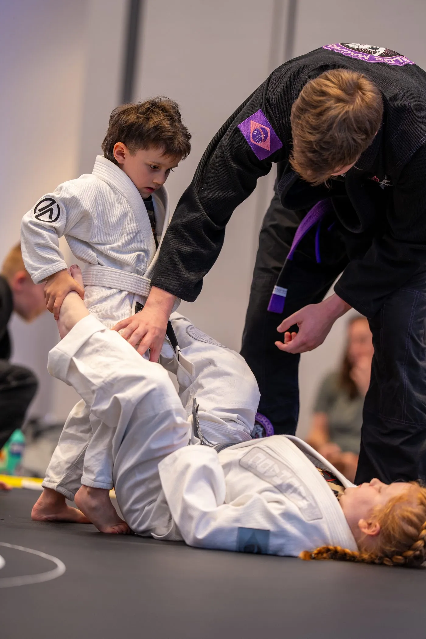 A young boy in a white gi and white belt drilling while a teenage coach guides his grip